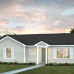 Single-story beige house with white trim and shutters, dark roof, and front door under a small overhang; walkway leads to the entrance, surrounded by grass, shrubs, and palm trees—showcasing custom homes Gainesville style at sunset.