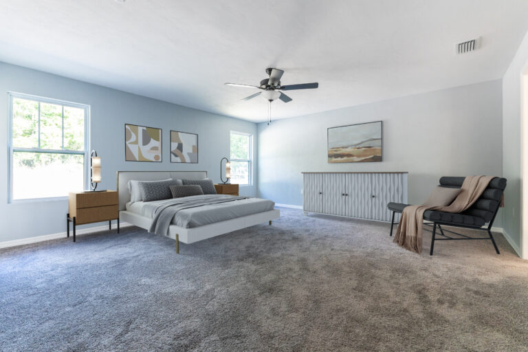Spacious bedroom with light gray carpet, a bed with gray bedding, two bedside tables, modern abstract art on blue-gray walls, a black lounge chair with a beige throw, and a ceiling fan—perfect for custom homes Gainesville owners. Natural light from two windows.