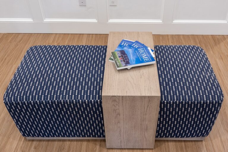 A rectangular blue and white patterned bench with a light wooden divider in the middle. On top of the divider are two magazines, both titled HOME, resting partially open. The bench is on a wooden floor.