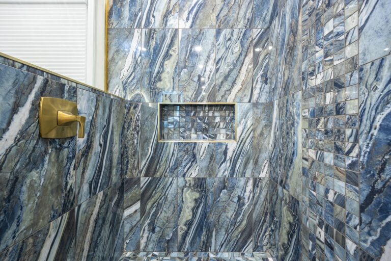 Shower interior with blue and gray marble tiles, a built-in niche, and a gold-tone handle on the left wall.