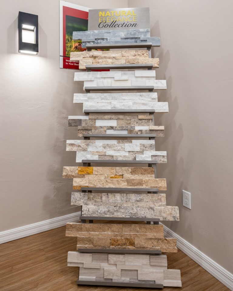 A display rack in a showroom holding various samples of stone or tile wall panels in different colors and textures, labeled Natural Elegance Collection, against a beige wall.