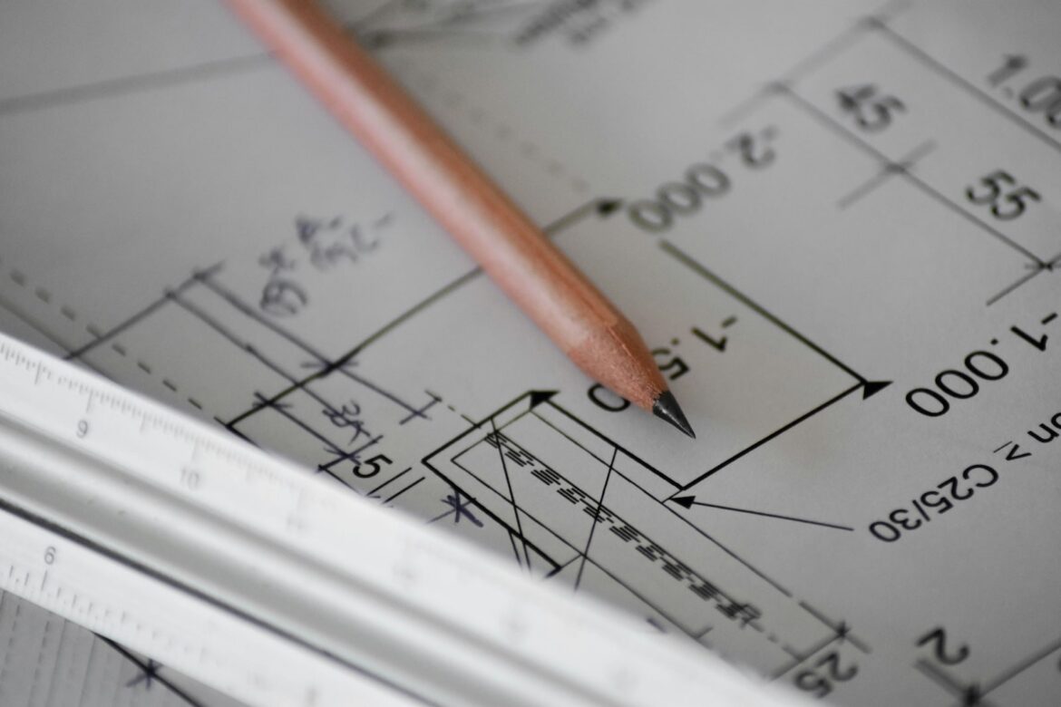 Close-up of a pencil resting on a technical blueprint with architectural measurements, alongside a white triangular ruler.